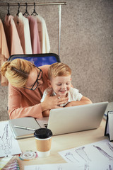 Happy businesswoman enjoying working in fashion studio with her little son