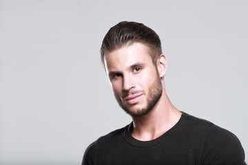 Fototapeta premium Muscular model young man with beard in black t-shirt on gray background. Fashion portrait of brutal sporty sexy strong muscle guy with modern trendy hairstyle. Model, fashion concept.