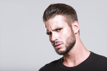 Fototapeta premium Muscular model young man with beard in black t-shirt on gray background. Fashion portrait of brutal sporty sexy strong muscle guy with modern trendy hairstyle. Model, fashion concept.