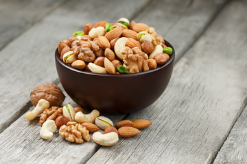 Fototapeta na wymiar Wooden bowl with mixed nuts on a wooden gray background. Walnut, pistachios, almonds, hazelnuts and cashews, walnut.