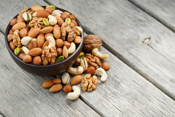 Wooden bowl with mixed nuts on a wooden gray background. Walnut, pistachios, almonds, hazelnuts and cashews, walnut.
