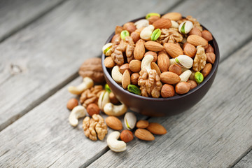 Wooden bowl with mixed nuts on a wooden gray background. Walnut, pistachios, almonds, hazelnuts and cashews, walnut.