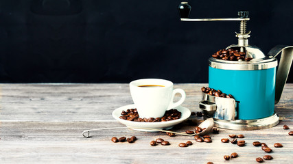 Coffee mill or grinder and cup of espresso. Concept of coffee drinking tradition. Selective focus. Wooden table. Black background. Copy space. 
