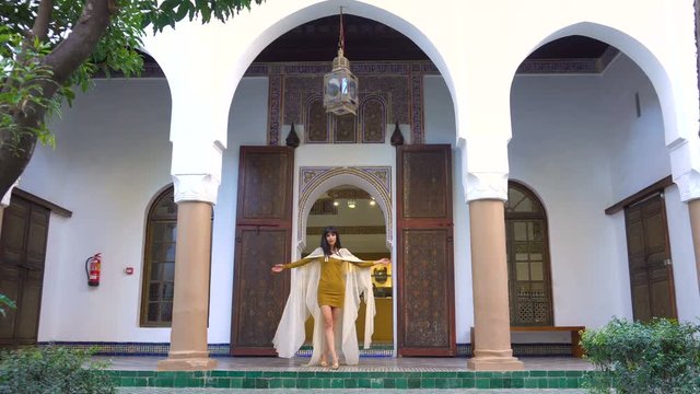 Beautiful Moroccan Girl Waving her white mantle in Picturesque Dar Si Said Riyad in Marrakech at sunset time