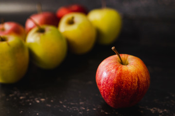 apples lines up and one red one standing out in front of them on its own
