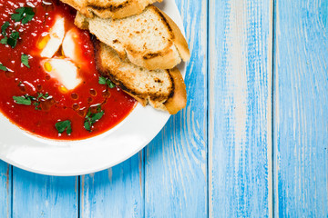 Tomato soup with mozzarella and toasts on wooden background