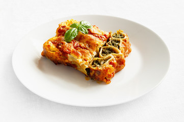 piece of baked in tomato and bechamell sauces cannelloni stuffed with spinach and beef decorated with basil