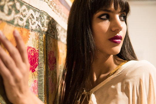 Beautiful Moroccan Girl in short golden dress and white mantle cloak in Rich interior of Picturesque Dar Si Said Riyad in Marrakech