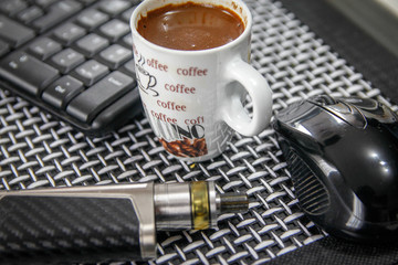Electronic cigarette, cup of coffee, computer mouse and keyboard on table in living room