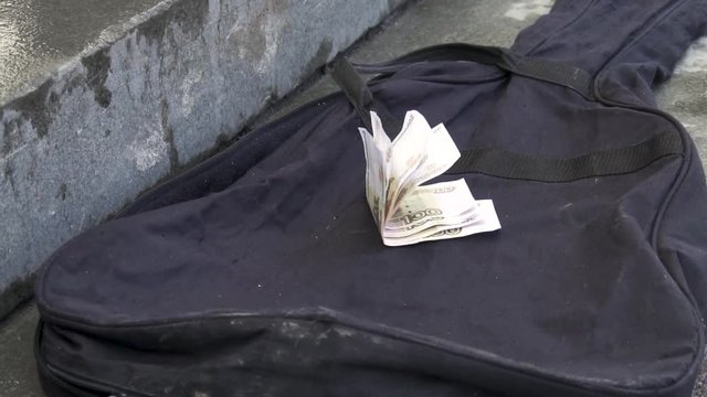 Close-up of the hand gives money as tip and put it on the case of the guitar. Street Musicians money in different currencies on the guitar case.