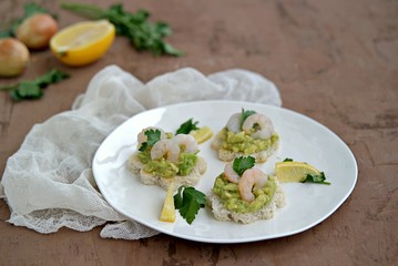 Small snack sandwiches on white bread with guacamole and shrimps on a white plate. Selective focus.