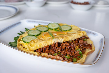 Omelet filled beef fried with vegetable on white table