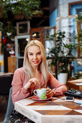 Portrait of a young attractive sexy blonde woman. The girl smiles and drinks a delicious hot drink in the cafe. Girl holding a Cup of coffee.