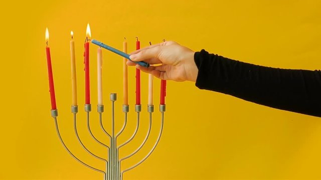 Hand lighting candles on a Hanukkah menorah - yellow background