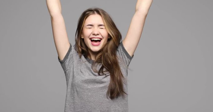 Young woman hope for something and get good result with win gesture isolated on gray background