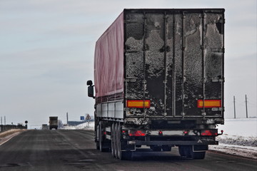 Back view on dirty european semi-trailer truck on asphalt winter road  - shipping, logistic, transport