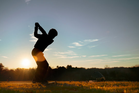 Young junior golfer practicing in a driving range with beautiful sunset light in winter.