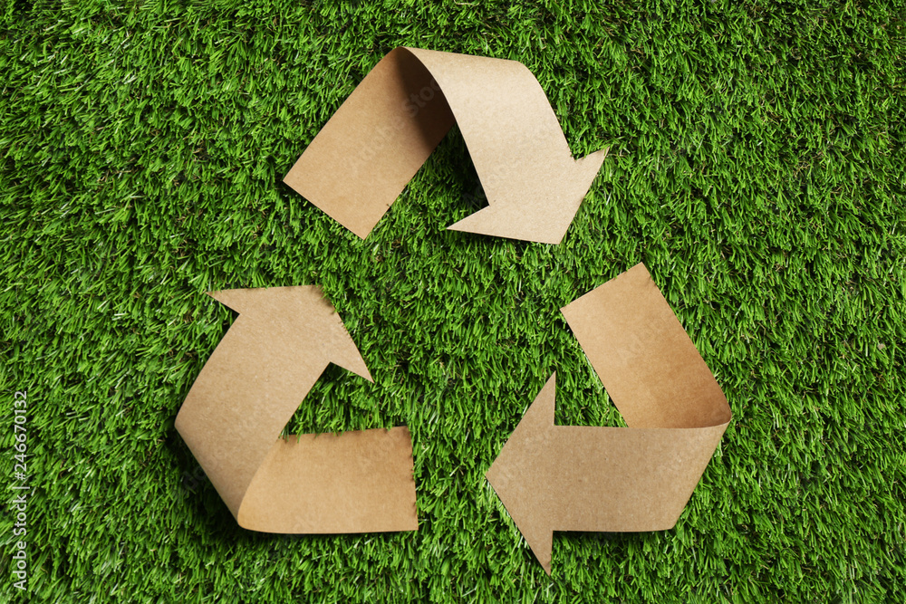 Wall mural recycling symbol cut out of kraft paper on green grass, top view