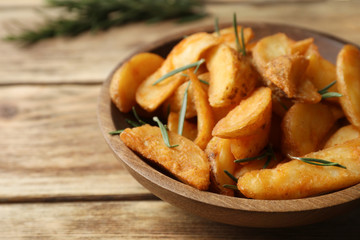 Plate with baked potatoes and rosemary on wooden table, closeup