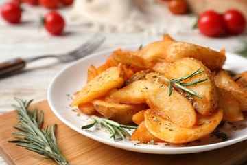 Plate with tasty baked potatoes and rosemary on wooden board
