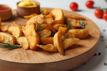 Wooden board with baked potatoes and rosemary on table, closeup