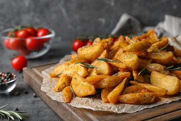 Wooden board with baked potatoes and rosemary on table