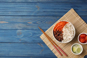 Flat lay composition with rice noodles and vegetables on wooden background. Space for text