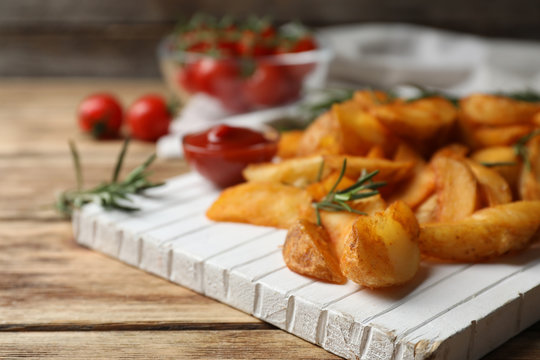 Wooden board with baked potatoes and rosemary on table, closeup