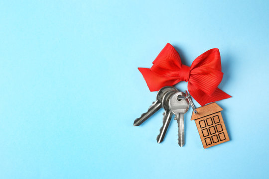 House keys with trinket and bow on color background, top view. Space for text