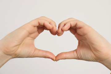 Young woman making heart with her hands on light background