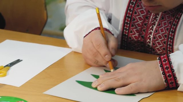 Boy with special needs outlines a Christmas tree on paper with a pencil. Rehabilitation for special children concept