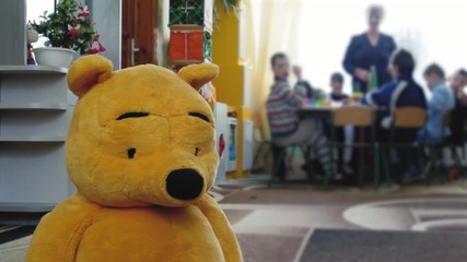 A group of children with special needs are playing in the children's boarding room. Teddy bear in the foreground. Rehabilitation for special children concept