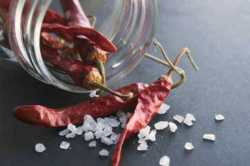 Red chili peppers in a mason jar, and sea salt on black background
