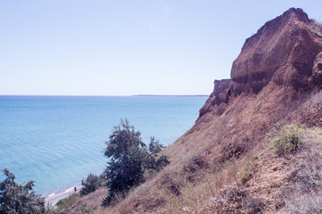 High cliff on the beach, in the summer afternoon, with greenery on the slope, from which far visible sea space with the coastline on the horizon, copy space, instagram.