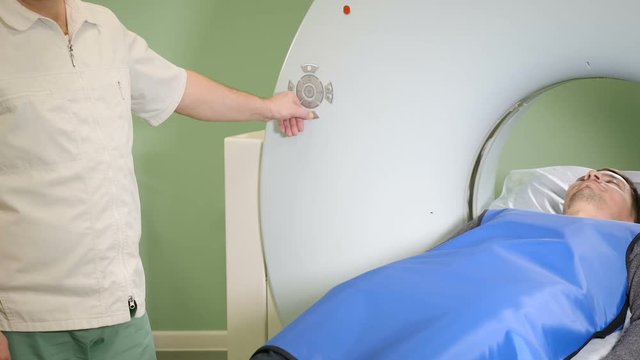 Male patient is moving into a CT-scanner. Medical equipment: computed tomography machine in diagnostic clinic. Health concept. Doctor presses settings button of CT MRI scanner. hd