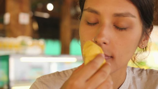 Young Tourist Woman Eating Durian First Time. Female Holding Piece of Durian Pulp and Sniffing It Enjoying Good Sweet Taste. 4K Slowmotion. Kuala Lumpur, Malaysia.