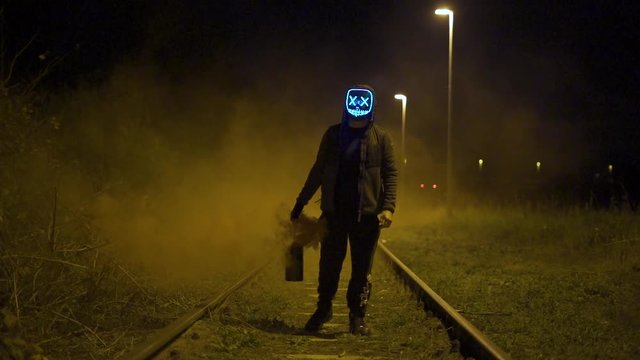 Man with glowing purge mask is holding a lantern with yellow smoke in slow motion.