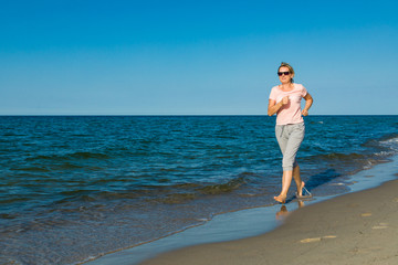 Fototapeta premium Middle-aged woman running on beach
