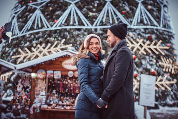 Fototapeta premium A happy young couple hold hands, enjoying spending time together, standing near a city Christmas tree