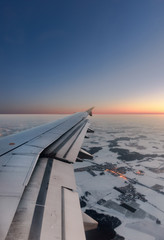 Fototapeta na wymiar Winter landing. Wing of an airplane with fully extended flaps overflying a snow-covered winter landscape at low altitude
