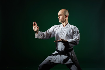 Against the background of dark green athlete performs formal karate exercises