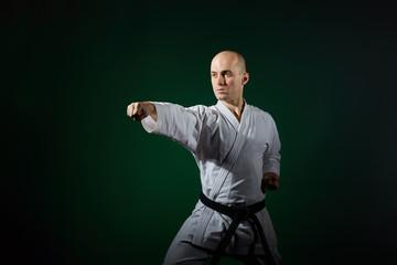Fototapeta premium Athlete doing formal karate exercises on a dark green background