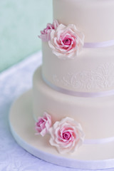 White three-tiered wedding cake with pink roses made of mastic stands on the table a delicate green background. letters bride and groom