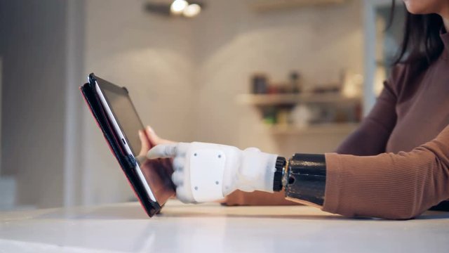 Tablet computer is getting operated by a female with a bionic arm