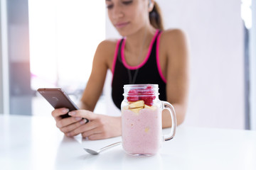 Strawberry and banana smoothie. In the background, sporty young woman using her mobile phone.