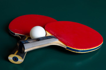 two ping-pong rackets and a ball on a green table.