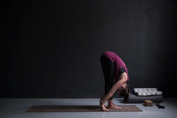 Sporty woman practicing yoga, standing forward bend exercise, uttanasana pose.