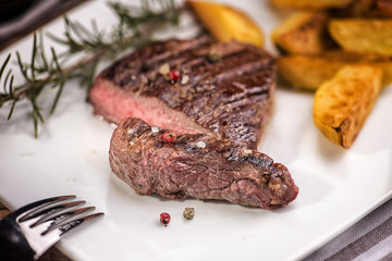 Beef steak with fried potatoes in slices on a white rectangular plate in a restaurant.