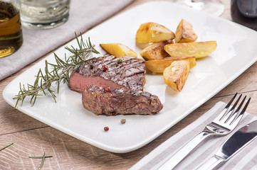 Beef steak with fried potatoes in slices on a white rectangular plate in a restaurant.