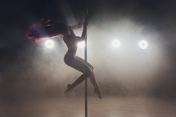 Naklejka na ściany i meble Young slim woman pole dancing in dark interior with lights and smoke.